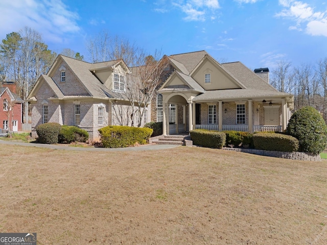 view of front of home featuring covered porch, brick siding, a chimney, and a front yard