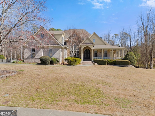 view of front facade with a porch, a front yard, and brick siding