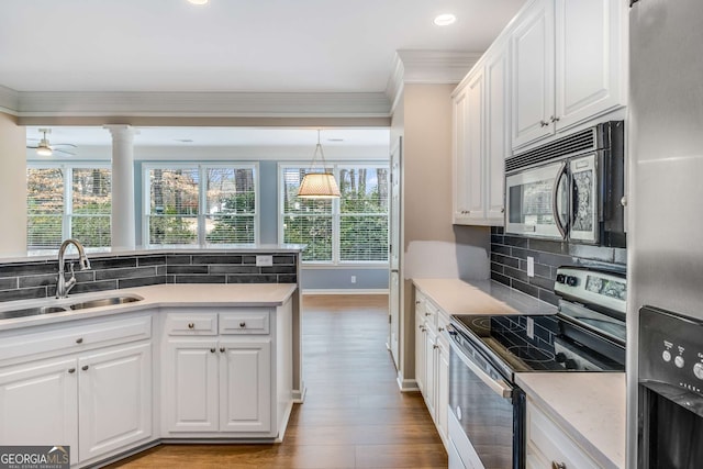 kitchen with crown molding, stainless steel appliances, white cabinets, a sink, and wood finished floors