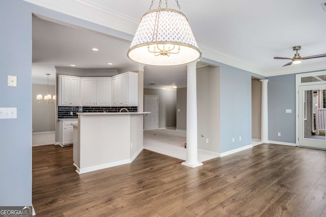 kitchen featuring decorative columns, backsplash, open floor plan, white cabinets, and ceiling fan with notable chandelier