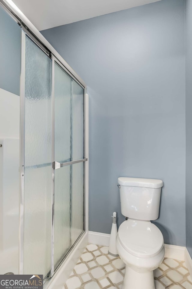 full bathroom with toilet, a shower stall, and baseboards