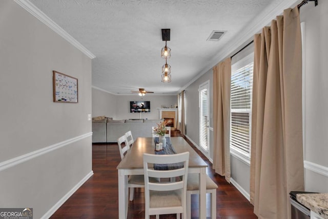 dining room featuring visible vents, dark wood-type flooring, a textured ceiling, crown molding, and a fireplace