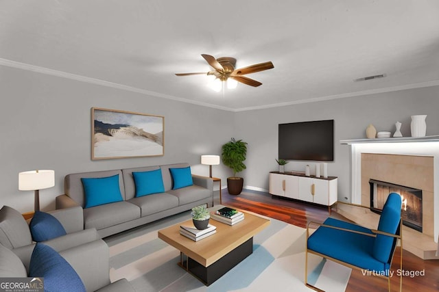 living area featuring ceiling fan, crown molding, a tiled fireplace, and wood finished floors