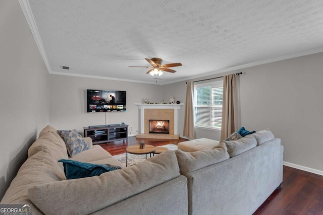 living room featuring dark wood-style flooring, a tiled fireplace, ornamental molding, a textured ceiling, and baseboards