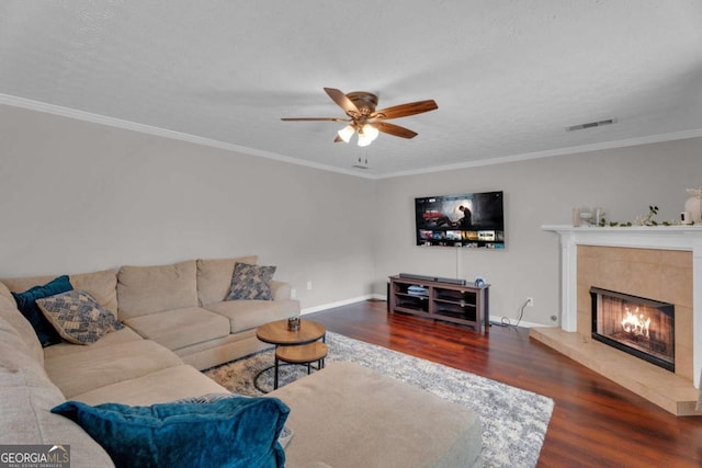 living area with a tile fireplace, crown molding, baseboards, and wood finished floors