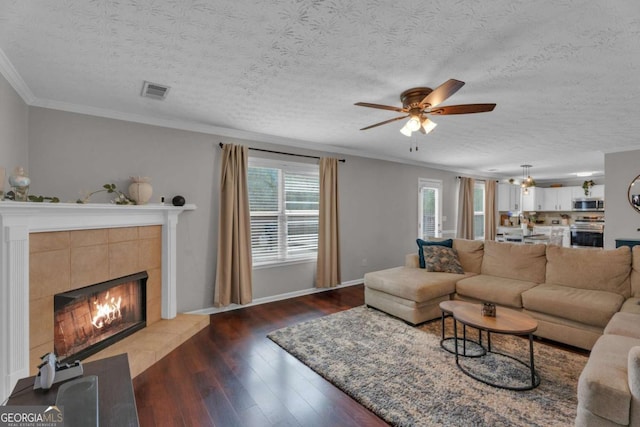 living room with ornamental molding, a tiled fireplace, dark wood finished floors, and visible vents