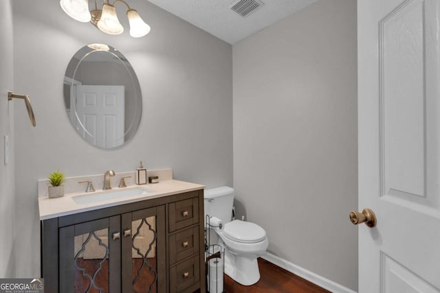 half bathroom featuring visible vents, toilet, wood finished floors, an inviting chandelier, and vanity