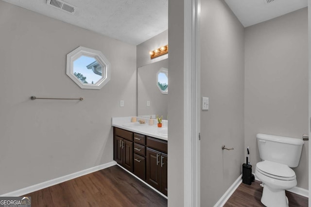 bathroom with baseboards, visible vents, toilet, wood finished floors, and a sink