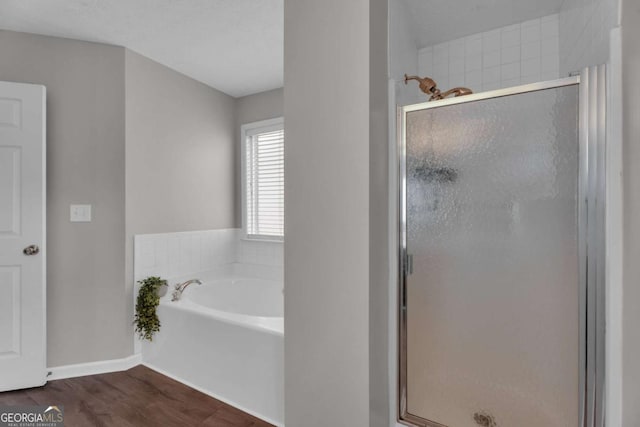 full bathroom featuring a garden tub, baseboards, wood finished floors, and a stall shower