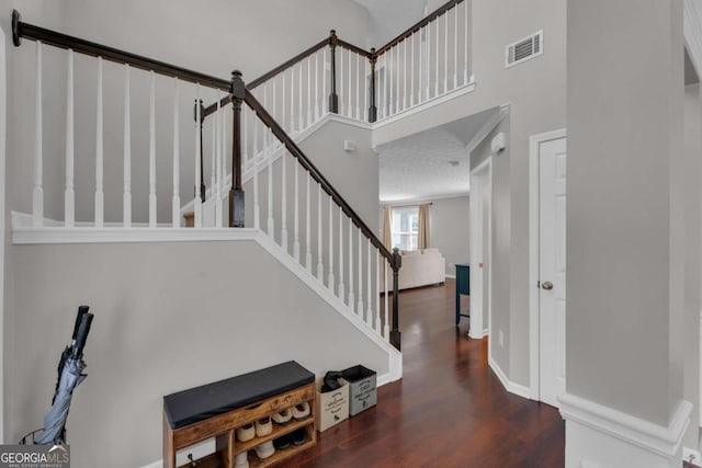 staircase with a high ceiling, wood finished floors, visible vents, and baseboards