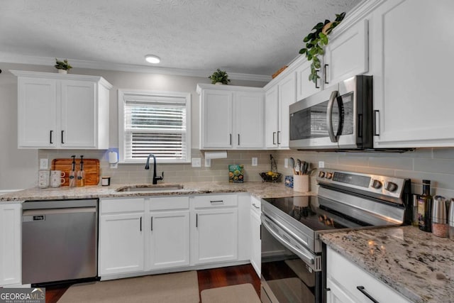 kitchen with stainless steel appliances, decorative backsplash, white cabinets, a sink, and light stone countertops