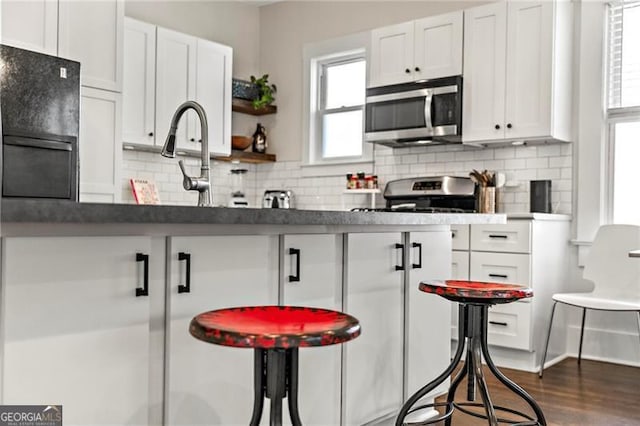 942 Byron Dr SW, Atlanta, GA 30310 - kitchen featuring appliances with stainless steel finishes, white cabinets, decorative backsplash, dark countertops, and a kitchen bar