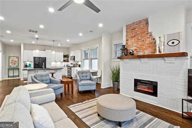 living room featuring a brick fireplace, dark wood-style floors, visible vents, and recessed lighting