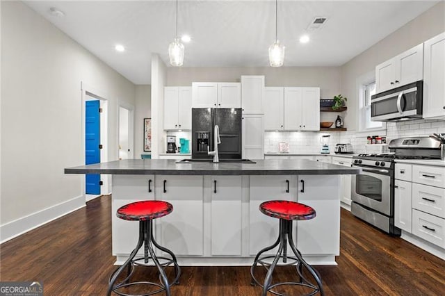 kitchen with appliances with stainless steel finishes, dark countertops, a sink, and a kitchen bar