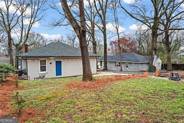 view of front of house with central AC, brick siding, roof with shingles, a front lawn, and a chimney