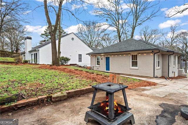 view of front of home featuring a patio, brick siding, and a shingled roof