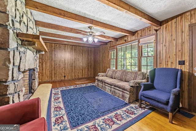 living room with wood-type flooring, wooden walls, beam ceiling, and a textured ceiling