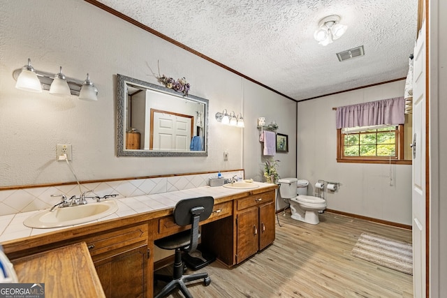 bathroom with toilet, wood finished floors, a sink, visible vents, and crown molding