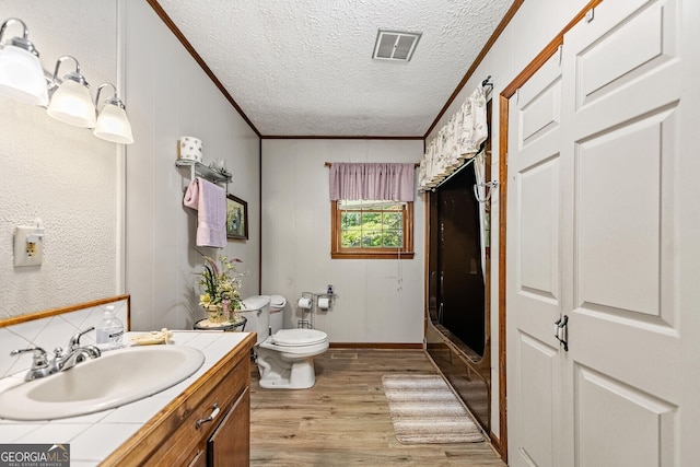 full bath featuring a textured ceiling, wood finished floors, vanity, visible vents, and crown molding