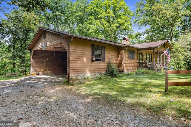 view of front of house with a chimney, covered porch, a garage, driveway, and a front lawn