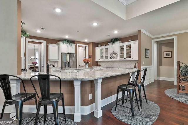 kitchen with stainless steel fridge, a kitchen bar, glass insert cabinets, and white cabinets