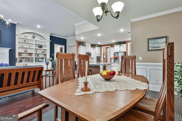 dining room with a decorative wall, wood finished floors, wainscoting, an inviting chandelier, and crown molding