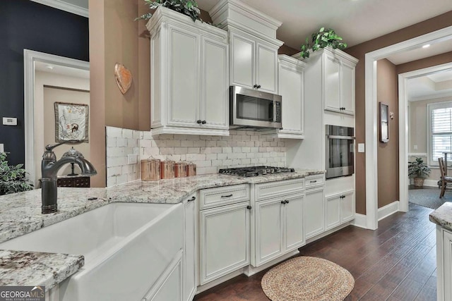 kitchen featuring dark wood finished floors, decorative backsplash, appliances with stainless steel finishes, a sink, and light stone countertops