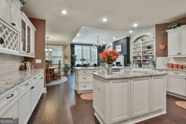 kitchen featuring a chandelier, a peninsula, dark wood-style flooring, white cabinets, and glass insert cabinets