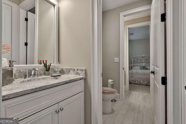 bathroom featuring baseboards, toilet, ensuite bath, wood finished floors, and vanity