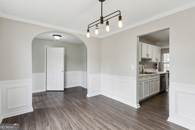 unfurnished dining area with dark wood finished floors, crown molding, arched walkways, and a sink