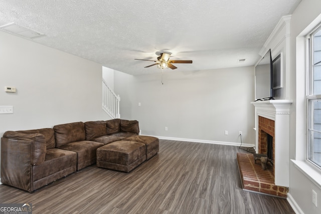 living area with a brick fireplace, baseboards, dark wood-style flooring, and a textured ceiling