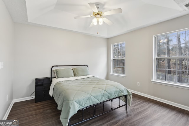 bedroom featuring baseboards, a raised ceiling, wood finished floors, and a ceiling fan