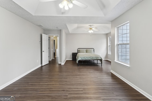 bedroom featuring a textured ceiling, baseboards, a tray ceiling, and dark wood-style flooring