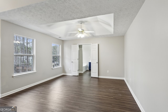 unfurnished bedroom featuring baseboards, a tray ceiling, ceiling fan, dark wood-type flooring, and a textured ceiling