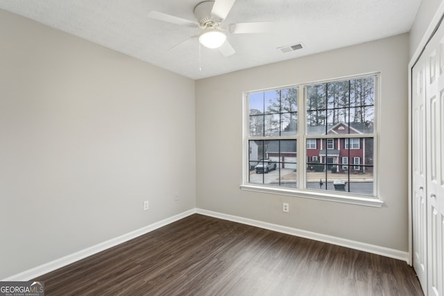 empty room featuring visible vents, ceiling fan, baseboards, dark wood finished floors, and a textured ceiling