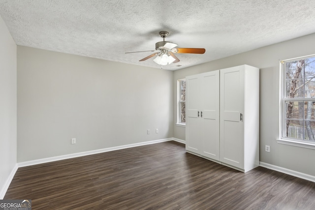 unfurnished bedroom with baseboards, a textured ceiling, dark wood finished floors, and a ceiling fan