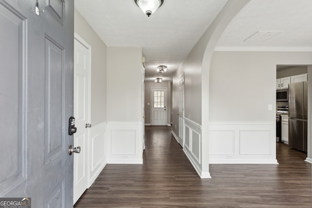 corridor featuring arched walkways, a decorative wall, a textured ceiling, and dark wood-type flooring