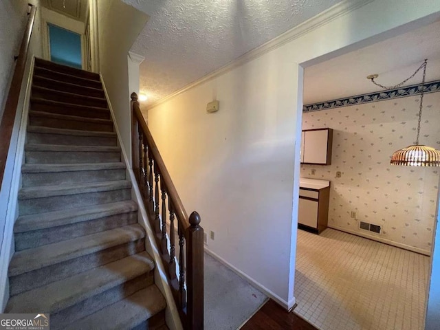 stairs featuring wallpapered walls, crown molding, baseboards, and a textured ceiling