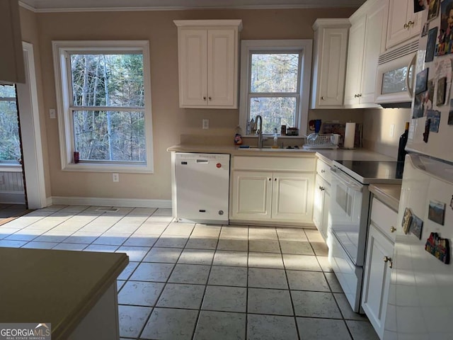 kitchen featuring white appliances, white cabinetry, a sink, and baseboards