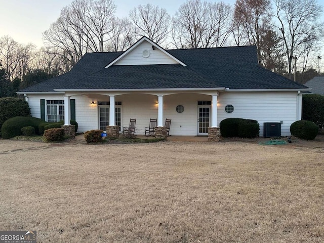 view of front of home featuring a shingled roof, cooling unit, covered porch, and a front lawn