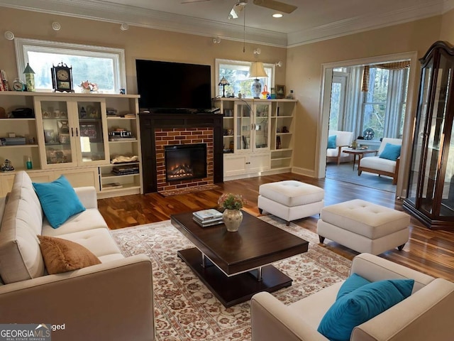 living room featuring a brick fireplace, wood finished floors, a wealth of natural light, and crown molding