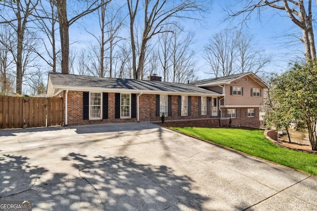 tri-level home with brick siding, fence, driveway, a chimney, and a front yard