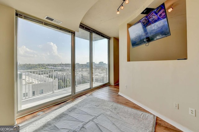 unfurnished room with wood finished floors, baseboards, visible vents, track lighting, and expansive windows