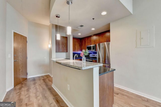 kitchen featuring appliances with stainless steel finishes, light stone countertops, light wood-type flooring, a peninsula, and baseboards