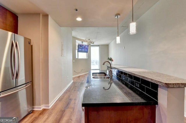 kitchen featuring light wood-style floors, freestanding refrigerator, a kitchen island with sink, a sink, and baseboards