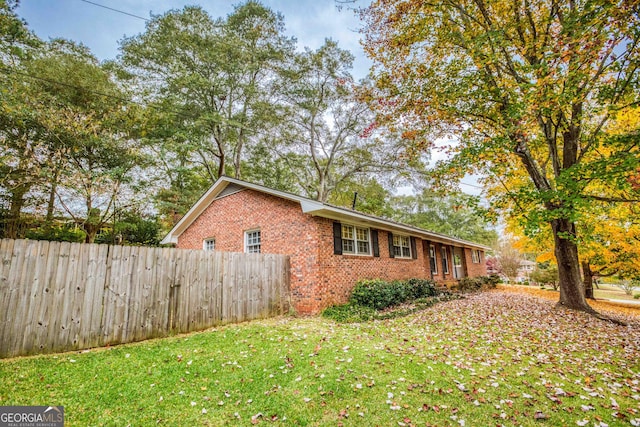 view of side of home with brick siding, fence, and a lawn