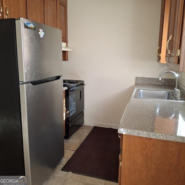 kitchen featuring black electric range, brown cabinets, freestanding refrigerator, a sink, and under cabinet range hood