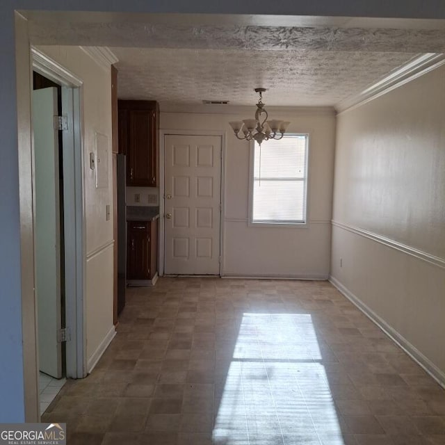 unfurnished dining area with crown molding, a textured ceiling, visible vents, and a notable chandelier