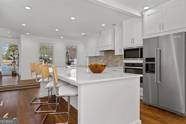 kitchen featuring decorative backsplash, dark wood-style floors, stainless steel appliances, premium range hood, and white cabinetry