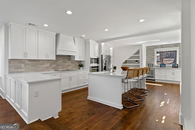 kitchen featuring beverage cooler, stainless steel appliances, premium range hood, visible vents, and dark wood-style floors